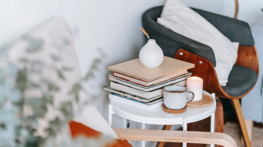 Cup of tea on coaster and flaming candle on wicker mat against textbooks and armchair in light house
